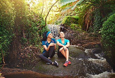 Buy stock photo Shot of two sporty young women taking a break while out exercising in nature