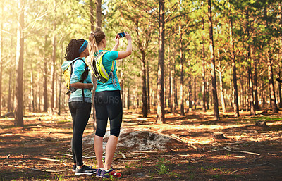 Buy stock photo Shot of two sporty young woman taking pictures while out in nature
