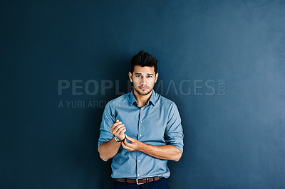 Buy stock photo Studio portrait of a handsome young businessman adjusting his wristwatch while standing against a grey background