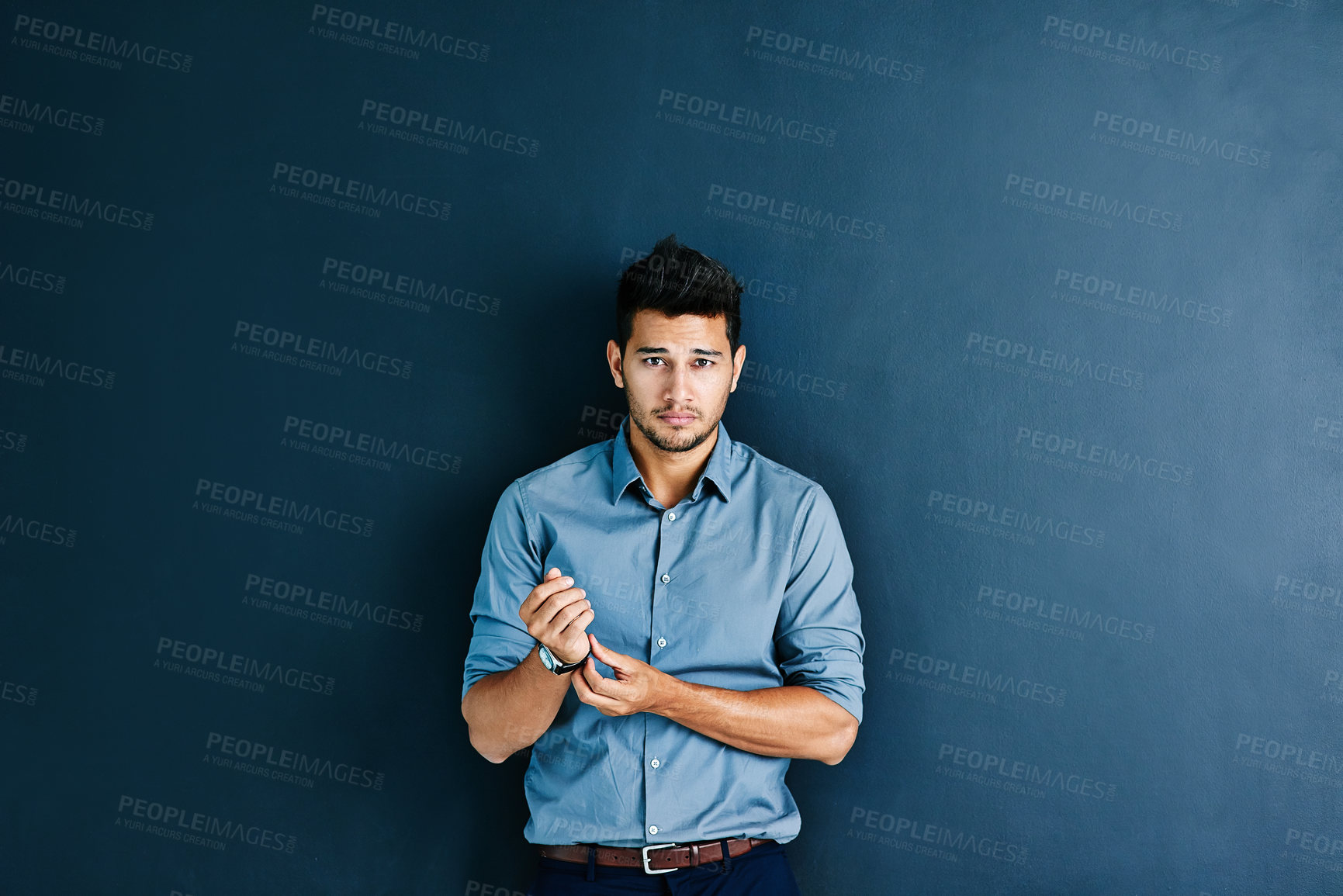 Buy stock photo Studio portrait of a handsome young businessman adjusting his wristwatch while standing against a grey background