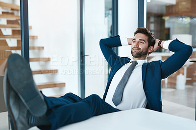 Buy stock photo Cropped shot of a handsome young businessman relaxing with his feet up on a desk in a modern office