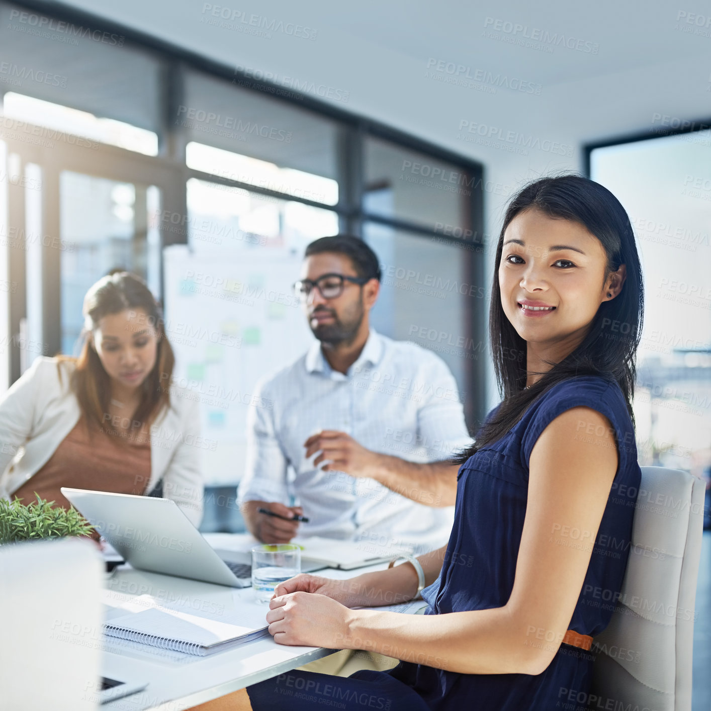 Buy stock photo Portrait of an attractive young businesswomen sitting in her office while her colleagues are having a discussion in the background