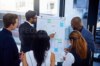 Buy stock photo Shot of a young businessman giving a demonstration on a white board to his colleagues in a modern office