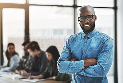 Buy stock photo Portrait of a cheerful businessman posing with his arms folded in a modern office with his colleagues in the background