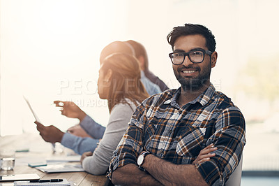 Buy stock photo Portrait of a confident young businessman sitting in on a meeting with colleagues in a modern office