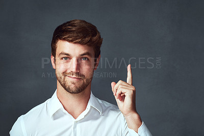 Buy stock photo Studio portrait of a handsome young man pointing to copyspace against a dark background