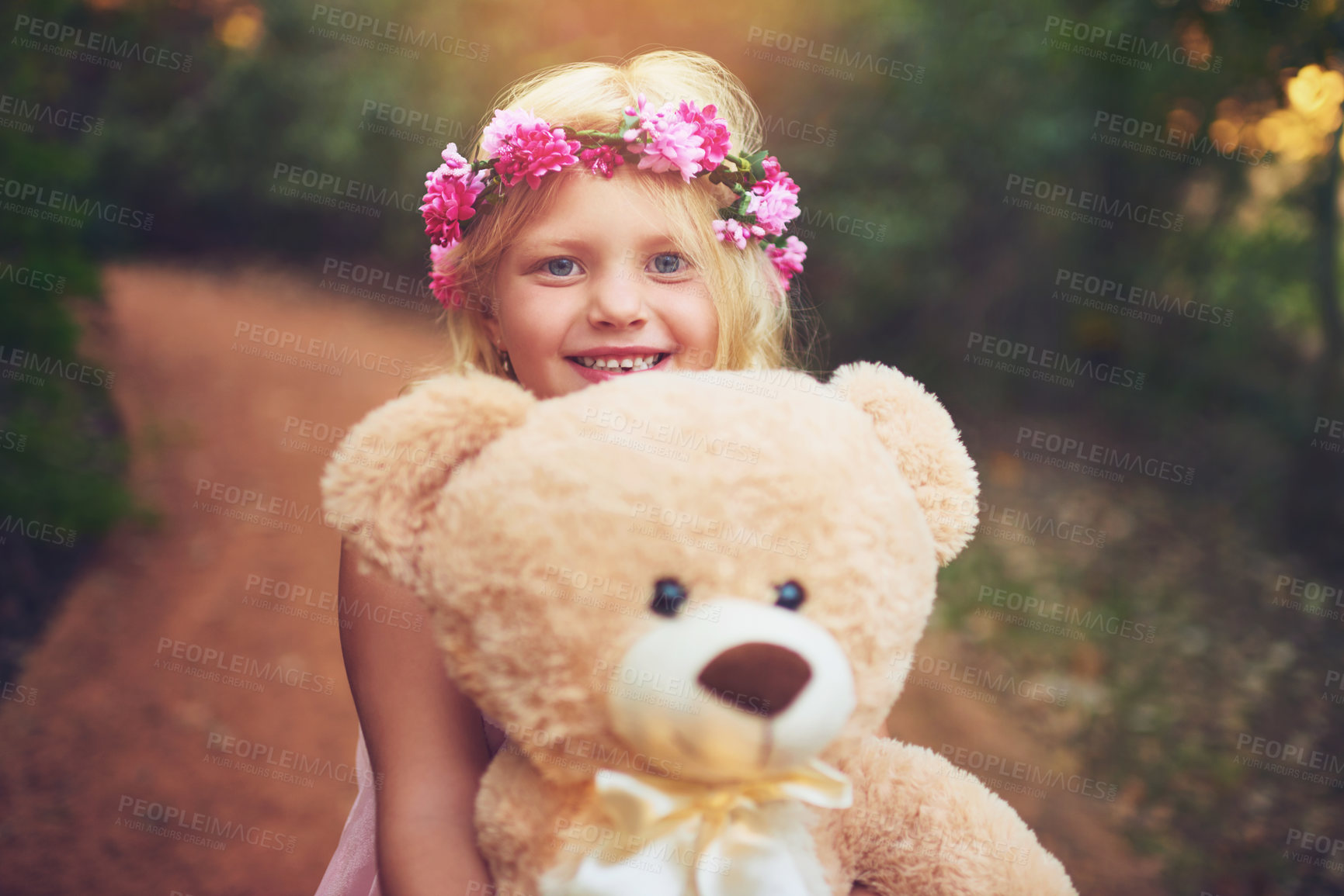Buy stock photo Shot of a happy little girl holding a teddy bear and looking at the camera while standing in the middle of a dirt road