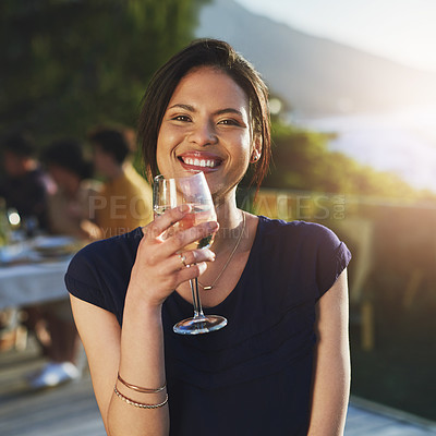 Buy stock photo Shot of an attractive young woman enjoying a glass of wine outdoors with her friends in the background