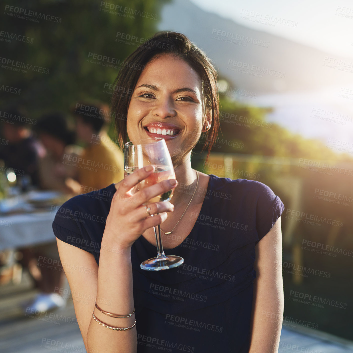 Buy stock photo Shot of an attractive young woman enjoying a glass of wine outdoors with her friends in the background