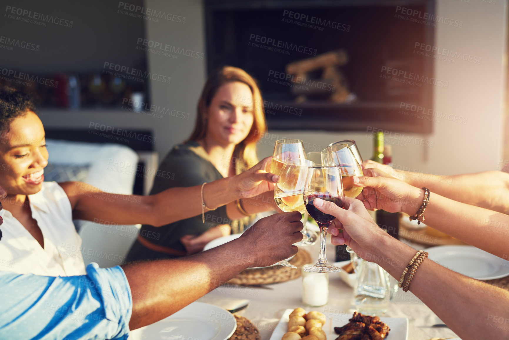 Buy stock photo Shot of a group of friends raising up their glasses for a toast while sitting around a table together outdoors