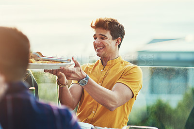 Buy stock photo Shot of a handsome young man being handed a plate of pasta to dish up at gathering with friends outdoors