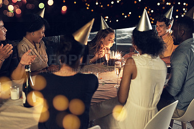 Buy stock photo Shot of a beautiful young woman blowing at the candles on her birthday cake at a evening gathering with friends