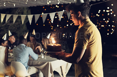Buy stock photo Shot of a handsome young man carrying a cake at a birthday celebration with friends outdoors in the evening
