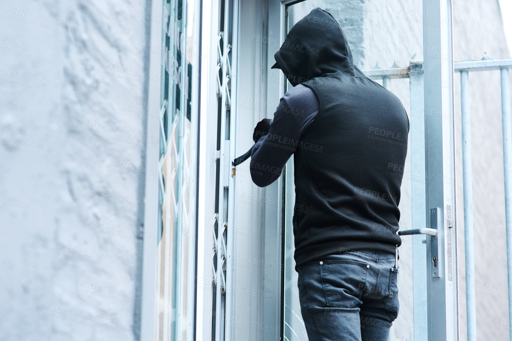 Buy stock photo Rearview shot of a male burglar using a steel weapon to break into a house