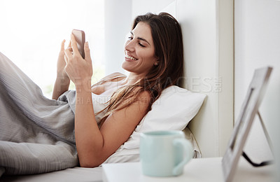 Buy stock photo Shot of a young woman using her cellphone while lying in bed