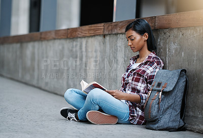 Buy stock photo Full length shot of an attractive young female student reading a book while sitting outside on campus