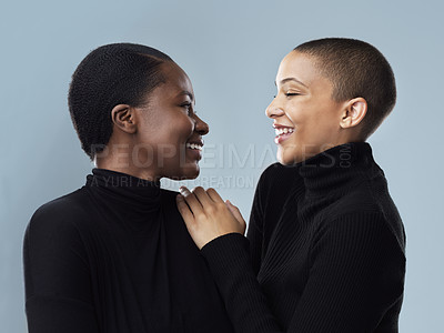 Buy stock photo Studio shot of two beautiful young women holding each other while standing against a grey background