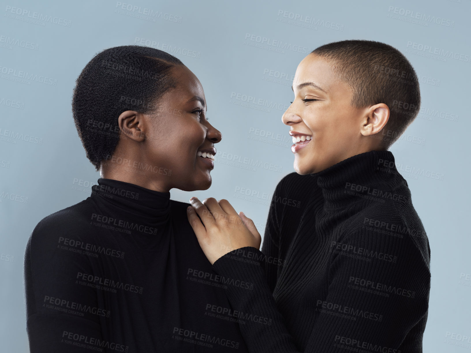 Buy stock photo Studio shot of two beautiful young women holding each other while standing against a grey background