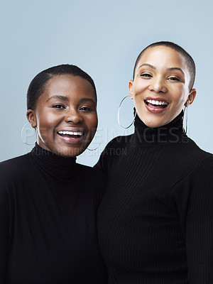 Buy stock photo Portrait of two beautiful young women holding each other while standing against a grey background