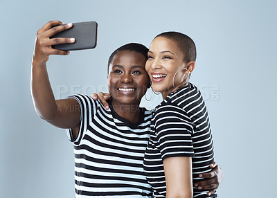 Buy stock photo Studio shot of two beautiful young women taking a selfie together against a grey background