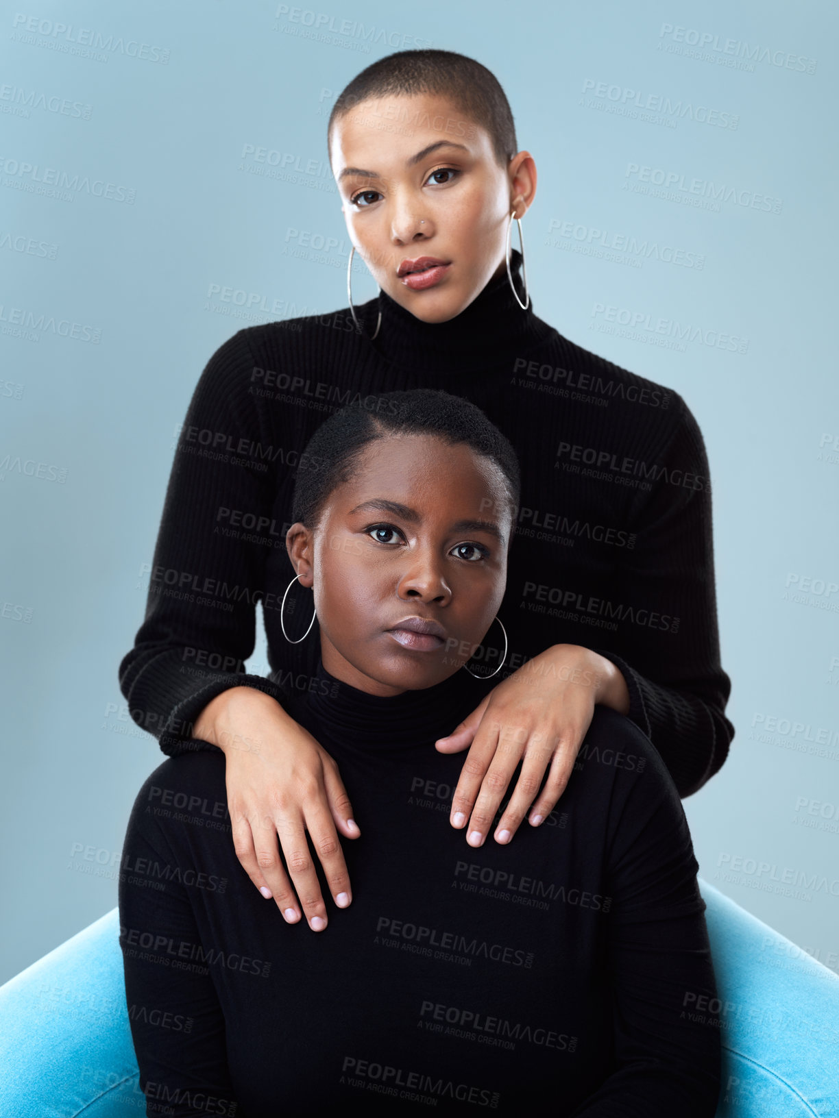 Buy stock photo Portrait of two beautiful young women holding each other while standing against a grey background