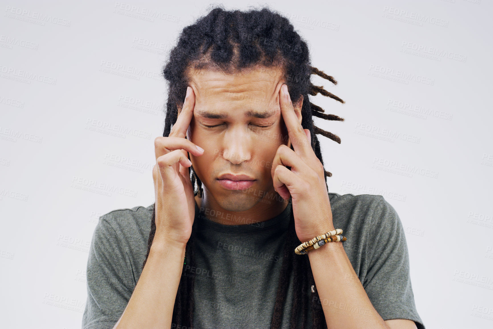Buy stock photo Shot of a young man holding his head while suffering from a headache against a grey background