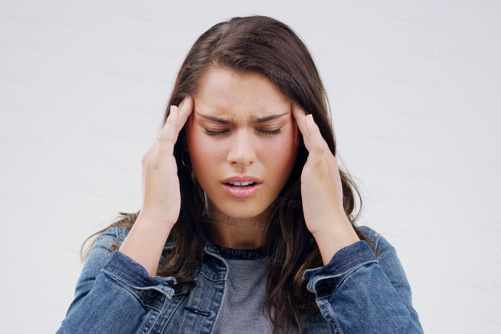 Buy stock photo Shot of a young woman holding her head while suffering from a headache against a grey background