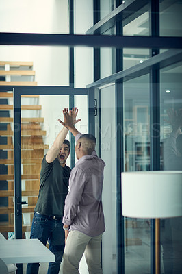 Buy stock photo Shot of two young businessmen giving each other a high five in a modern office