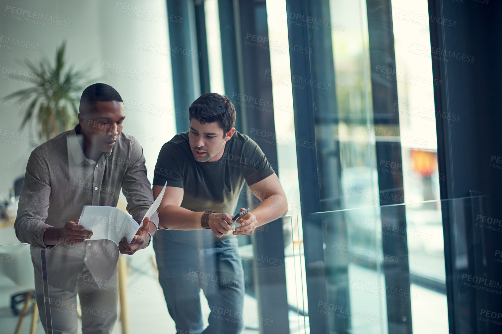 Buy stock photo Shot of two young businessmen going over paperwork together in a modern office