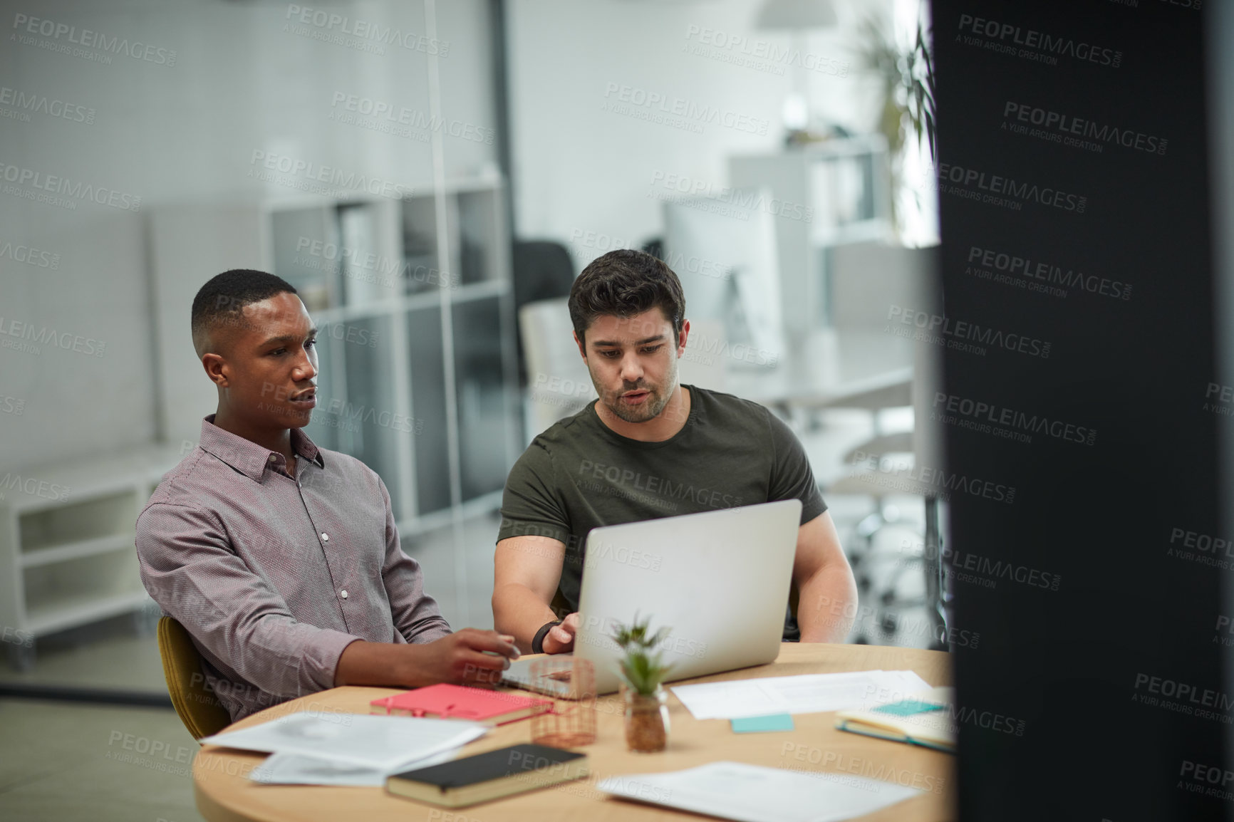 Buy stock photo Shot of two young businessmen using a laptop during a meeting in a modern office