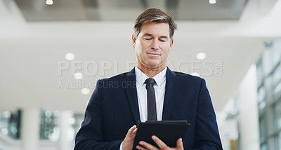 Buy stock photo Cropped shot of a mature businessman using a digital tablet while walking through a modern office