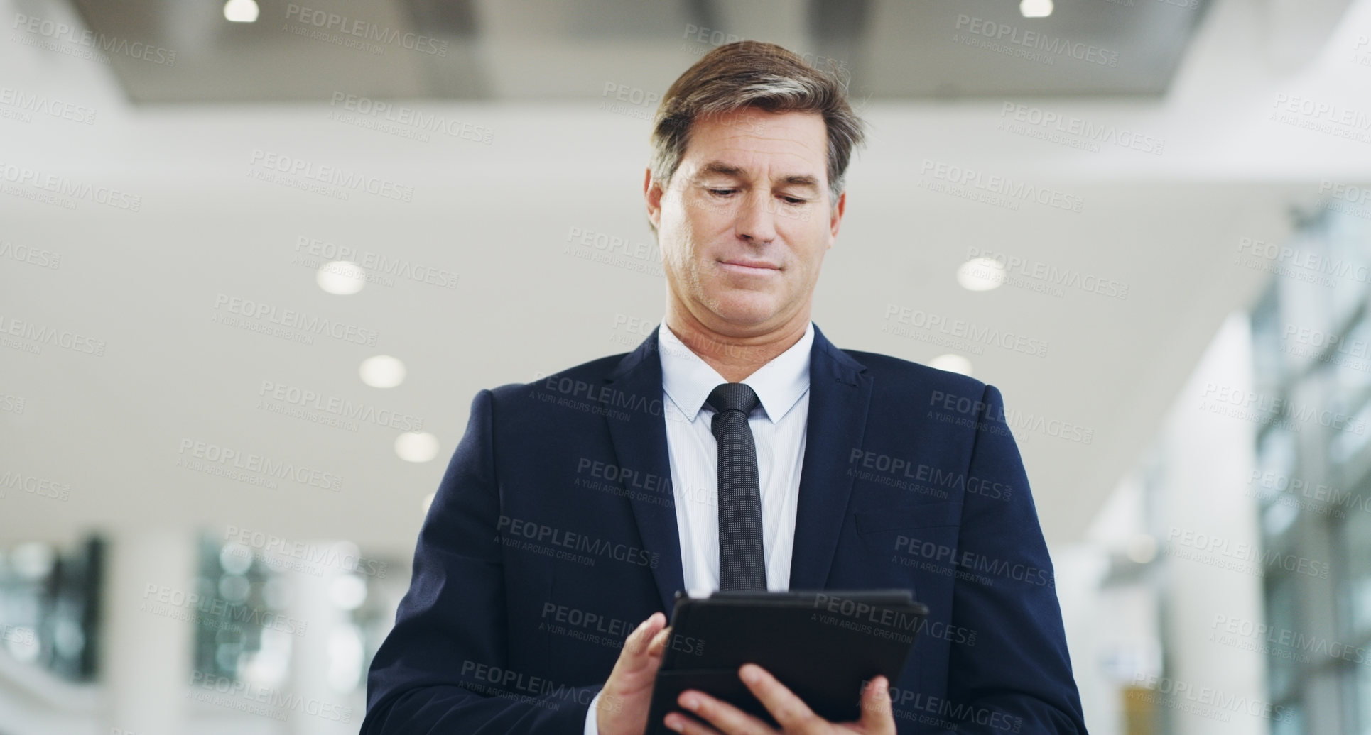 Buy stock photo Cropped shot of a mature businessman using a digital tablet while walking through a modern office