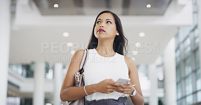 Buy stock photo Cropped shot of a young businesswoman using a smartphone while walking through a modern office