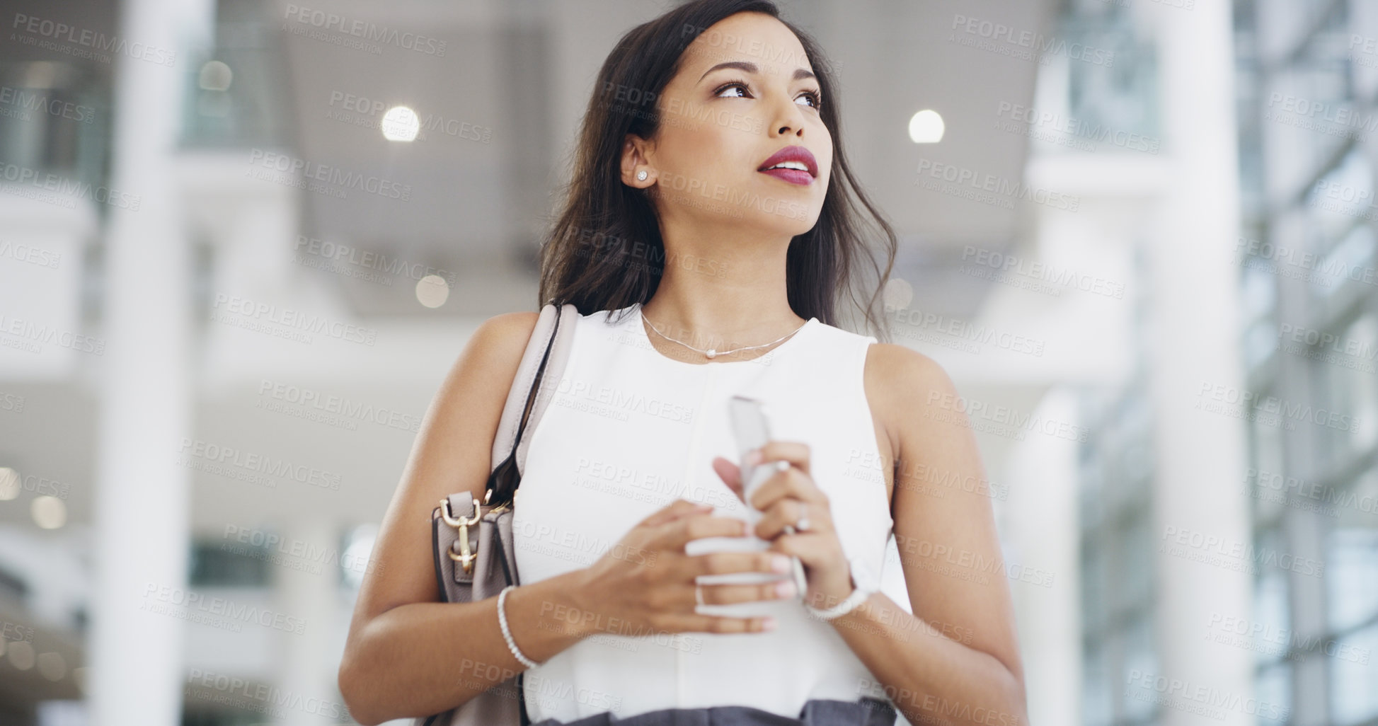 Buy stock photo Cropped shot of a young businesswoman using a smartphone while walking through a modern office