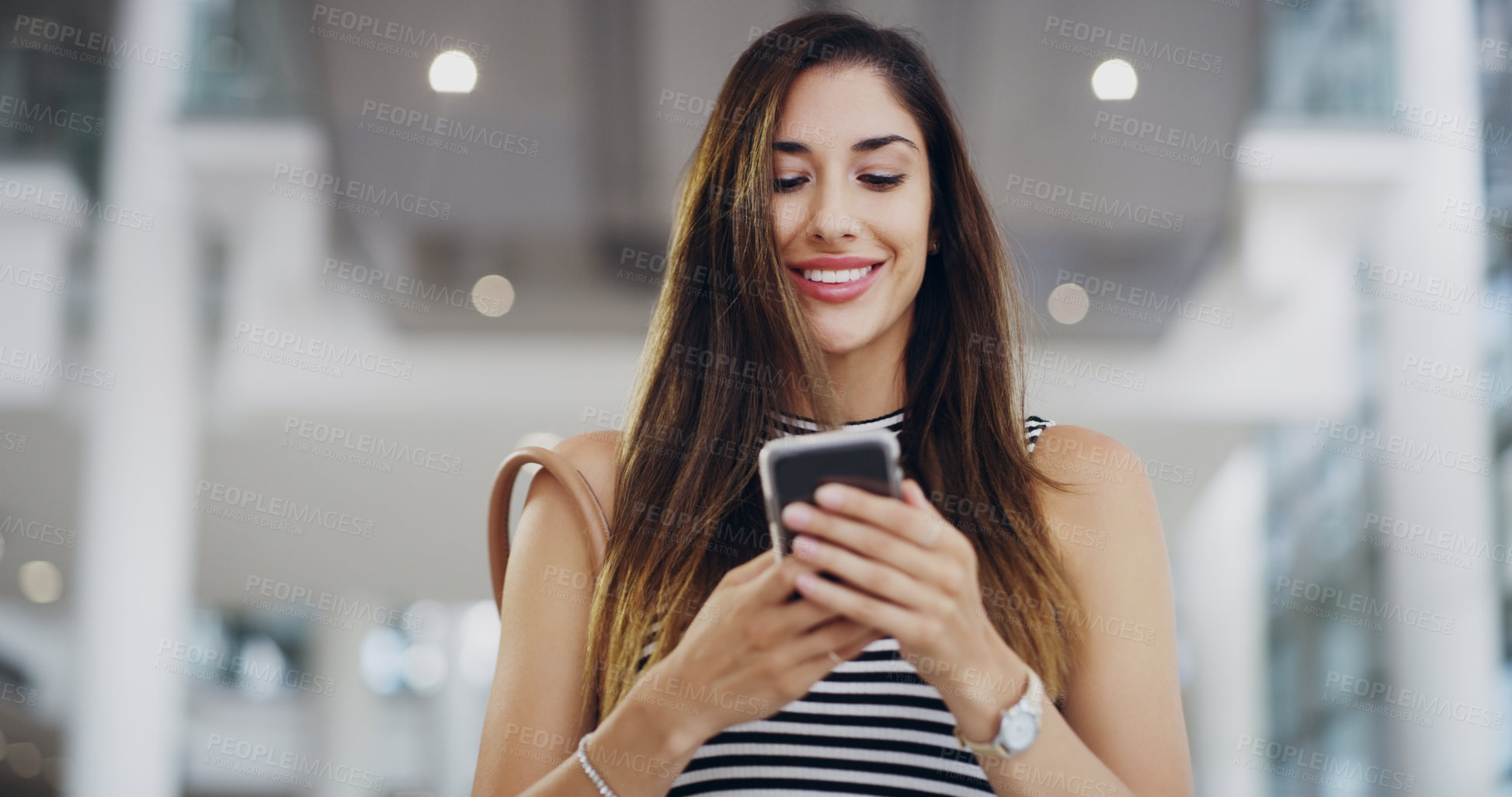 Buy stock photo Cropped shot of a young businesswoman using a smartphone while walking through a modern office