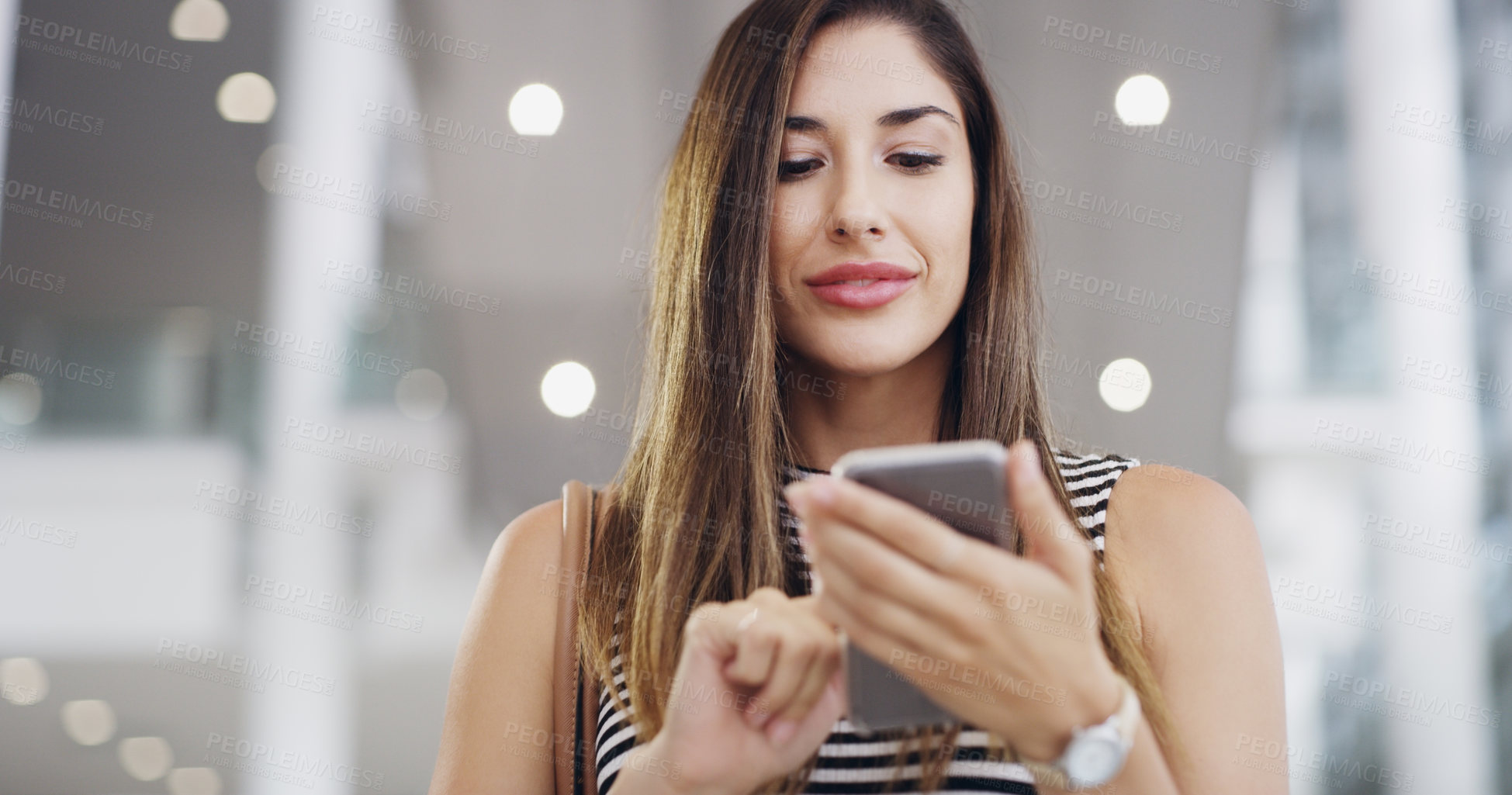 Buy stock photo Cropped shot of a young businesswoman using a smartphone while walking through a modern office