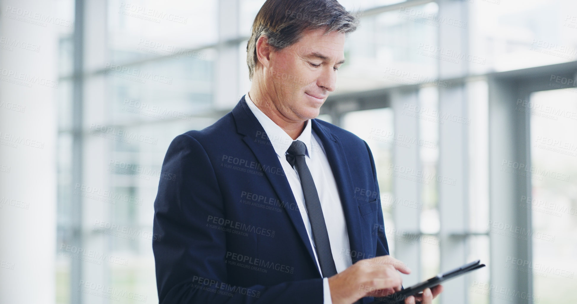 Buy stock photo Cropped shot of a mature businessman using a digital tablet while walking through a modern office