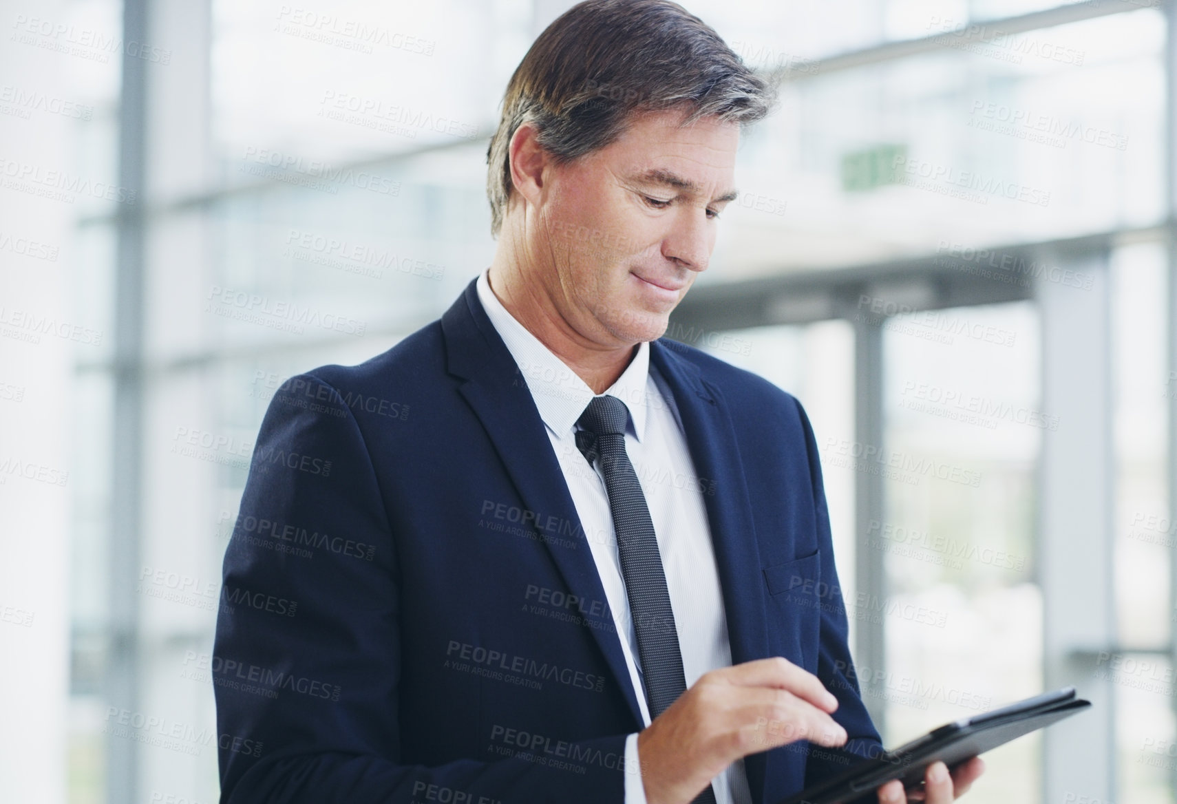 Buy stock photo Cropped shot of a mature businessman using a digital tablet while walking through a modern office
