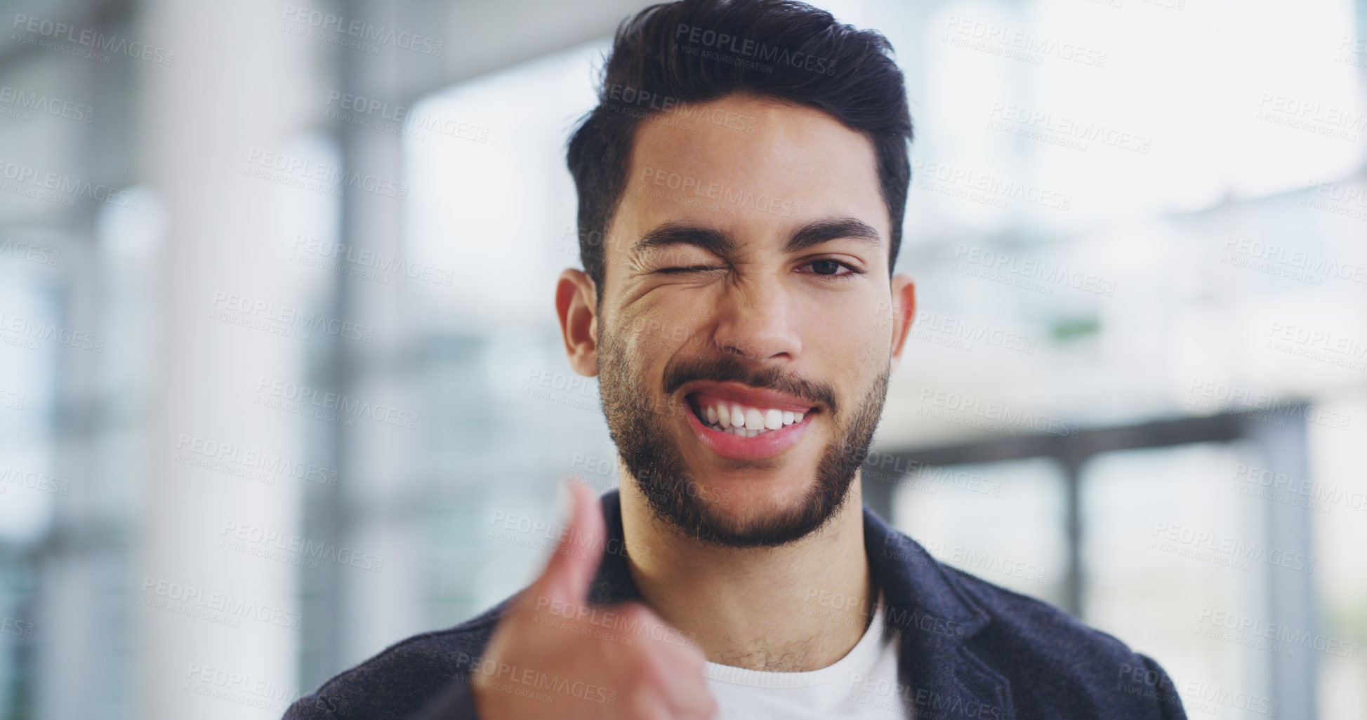 Buy stock photo Cropped shot of a young businessman showing winking and showing thumbs up while walking through a modern office