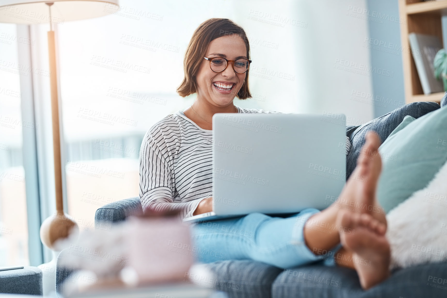Buy stock photo Full length shot of a happy young woman using a laptop while relaxing in her living room