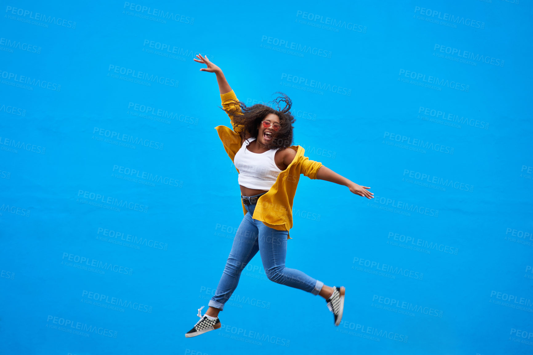 Buy stock photo Full length shot of a happy young woman jumping into the air against a blue background