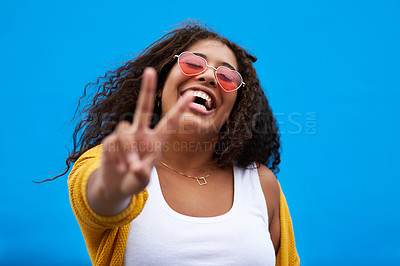 Buy stock photo Cropped shot of a young woman showing the peace sign against a blue background