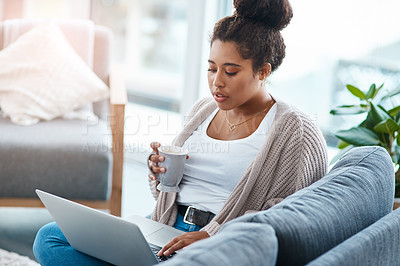 Buy stock photo Cropped shot of an attractive young woman using her laptop while having coffee in her living room