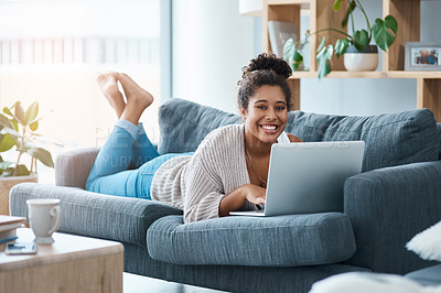 Buy stock photo Full length portrait of a happy young woman using her laptop while laying on the sofa at home