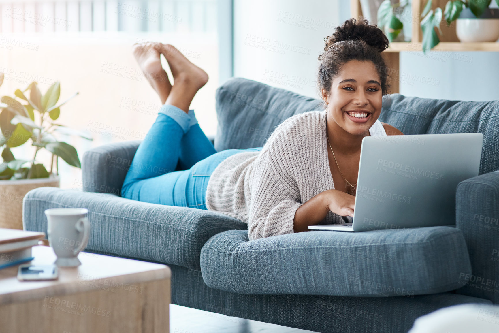 Buy stock photo Full length portrait of a happy young woman using her laptop while lying on the sofa at home