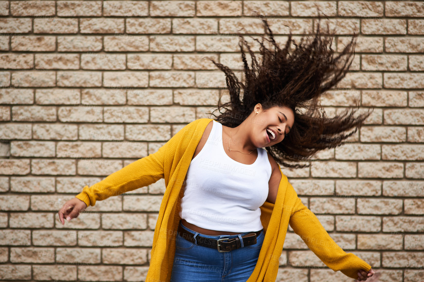 Buy stock photo Cropped shot of a happy young woman dancing against a brick wall