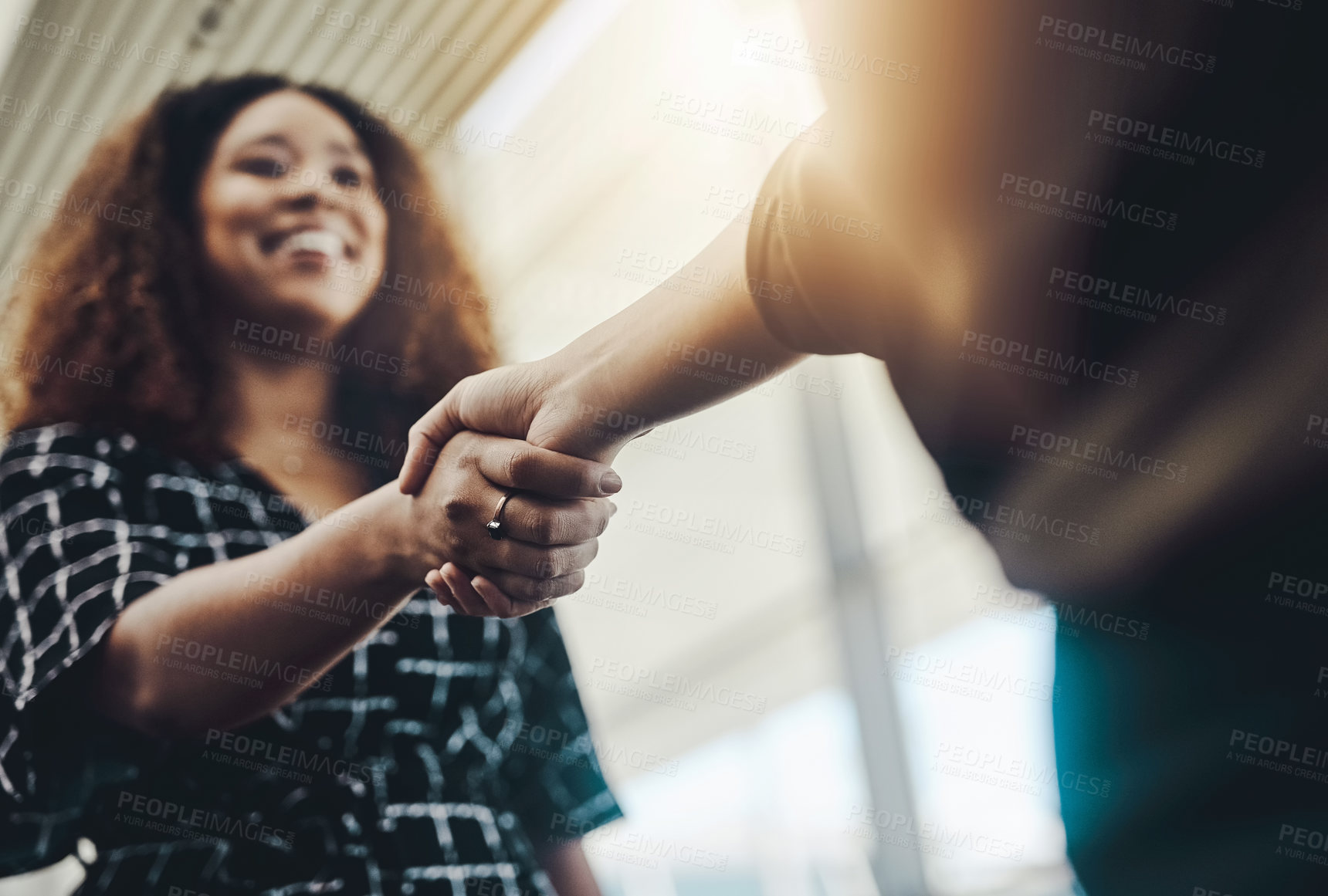 Buy stock photo Low angle shot of an attractive young businesswoman shaking hands with an associate in a modern workplace