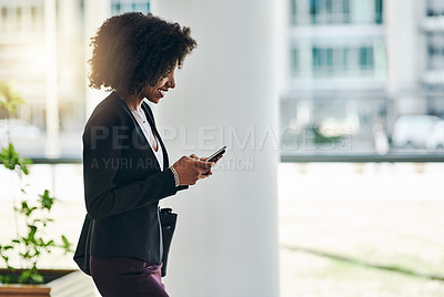 Buy stock photo Shot of a confident young businesswoman texting on her phone while standing in the office at work