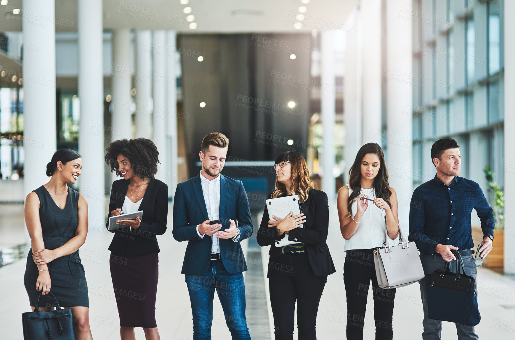 Buy stock photo Shot of a group of confident young businesspeople standing in a row next to each other inside of the office during the day