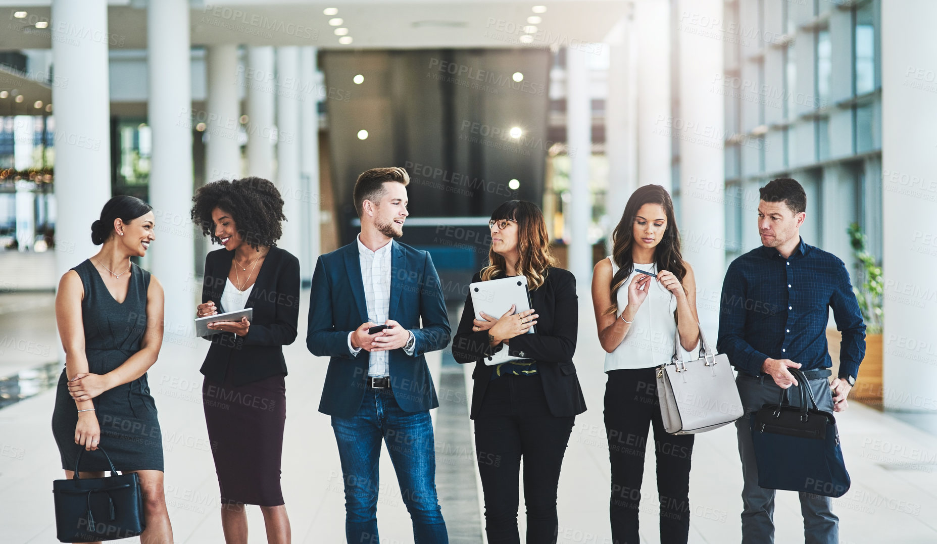 Buy stock photo Shot of a group of confident young businesspeople standing in a row next to each other inside of the office during the day